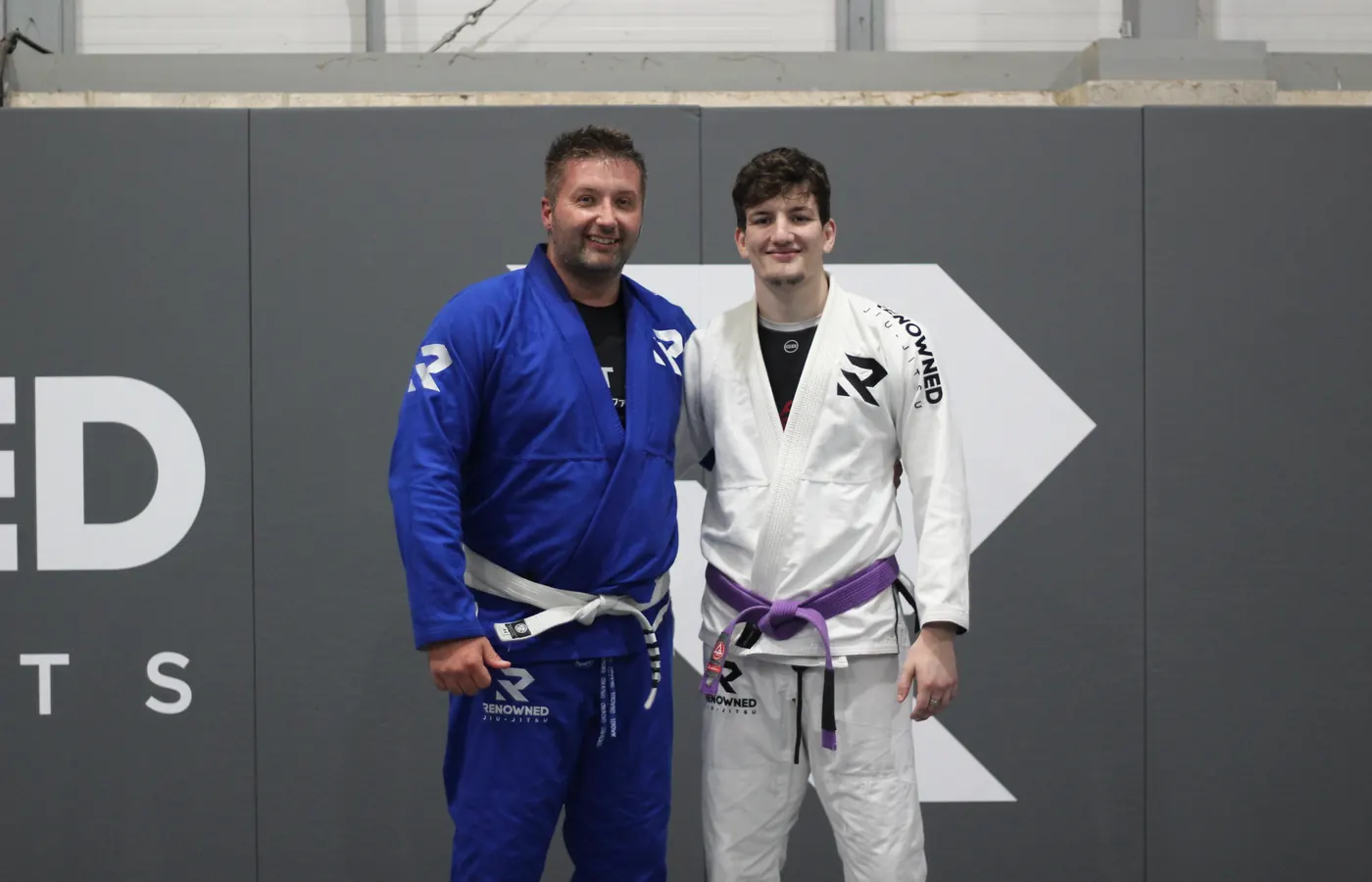 A coach and a student standing together on the mats after a class