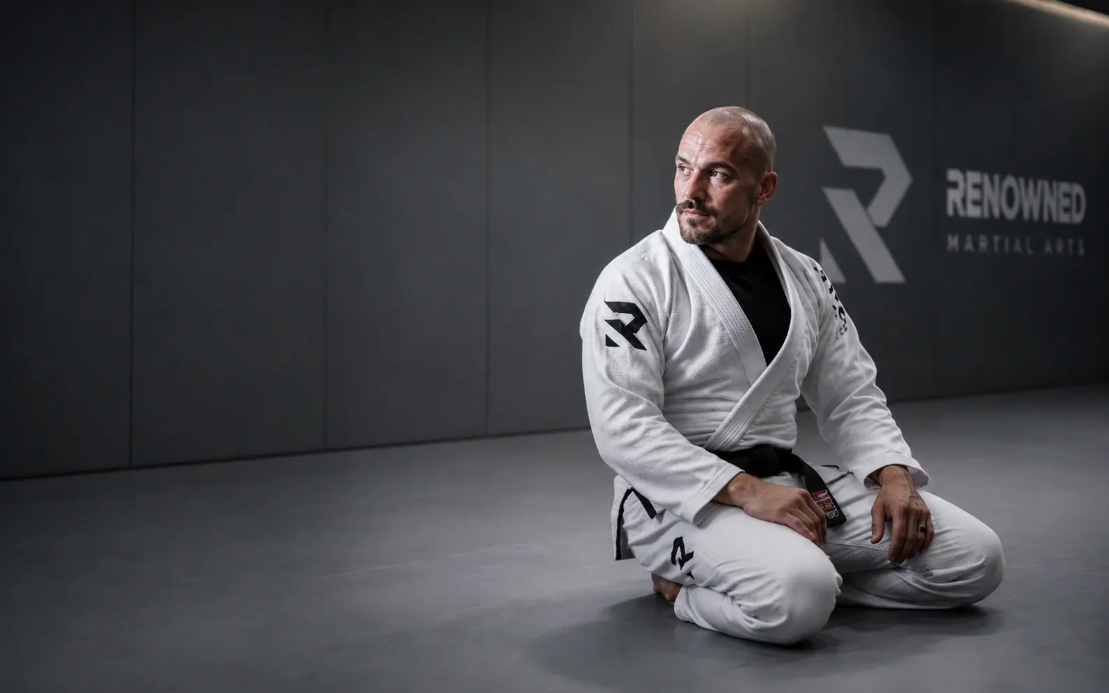 A black belt kneeling on the mats at Renowned Martial Arts, the academy wall behind him