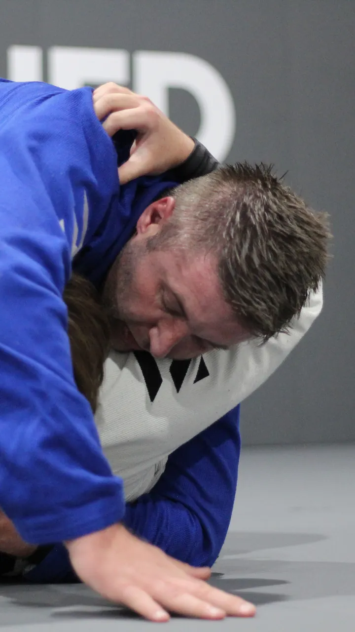 Two adults training jiu jitsu in gis, one working to pass the other's guard
