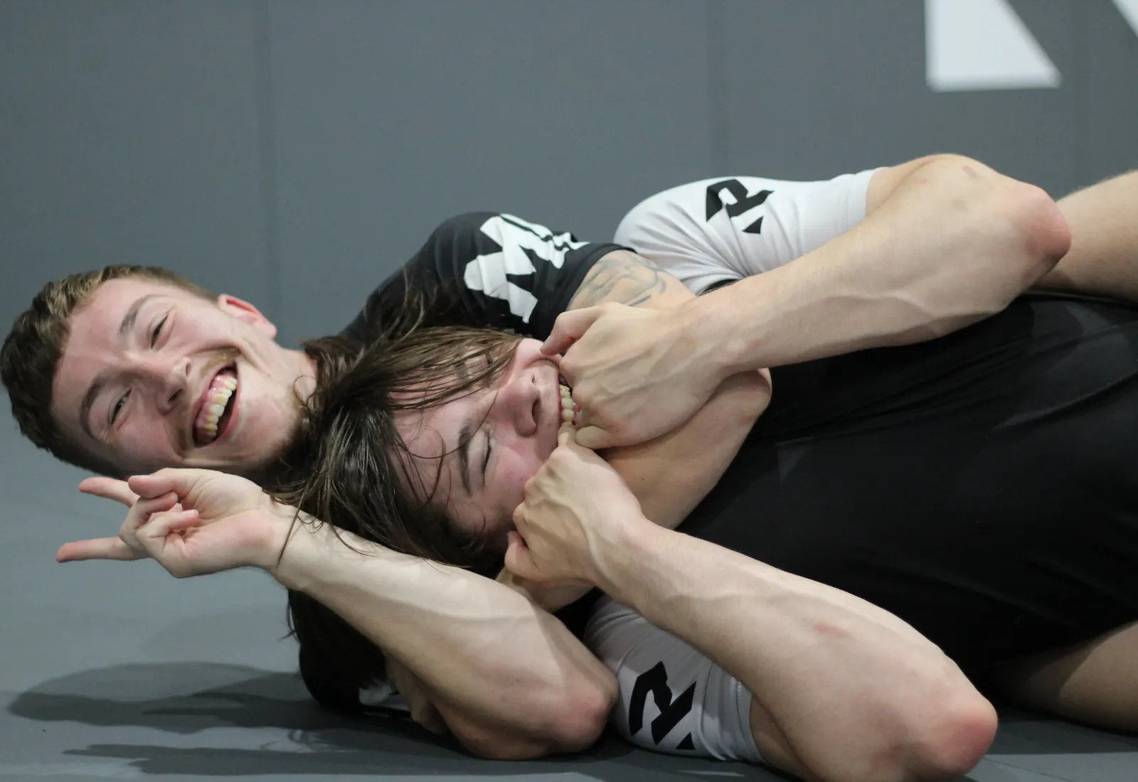 Two students laughing partway through a round of jiu jitsu