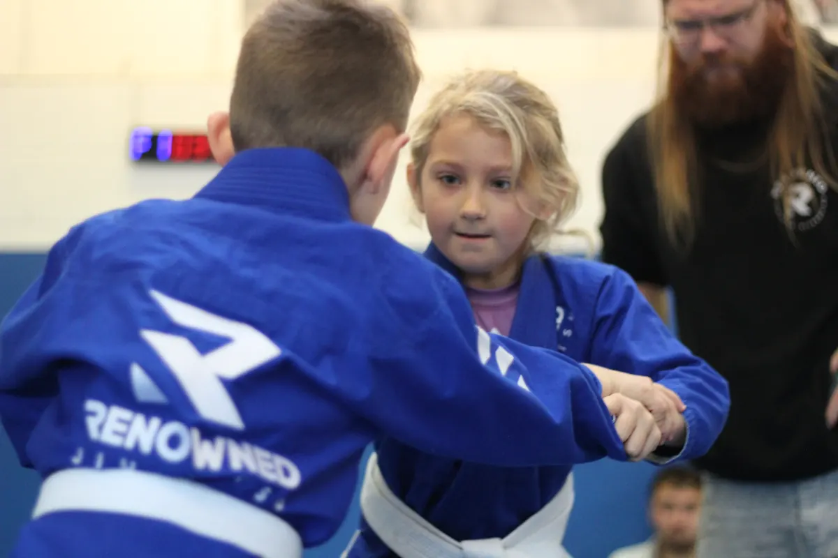 Two young children taking grips while a coach kneels beside them