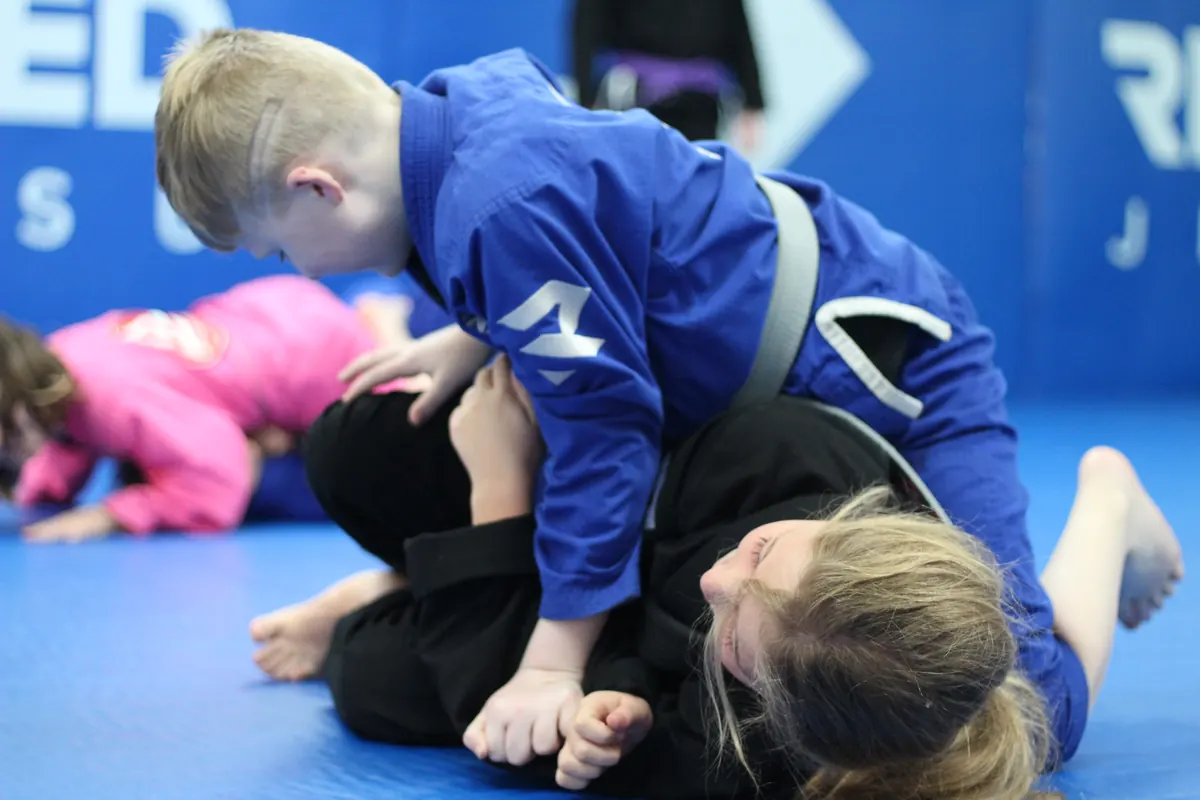 A child in a blue gi holding a top position in a kids class