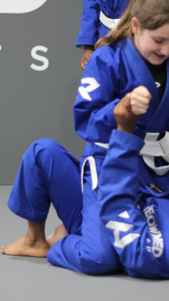 A child in a blue gi working a position in a kids jiu jitsu class