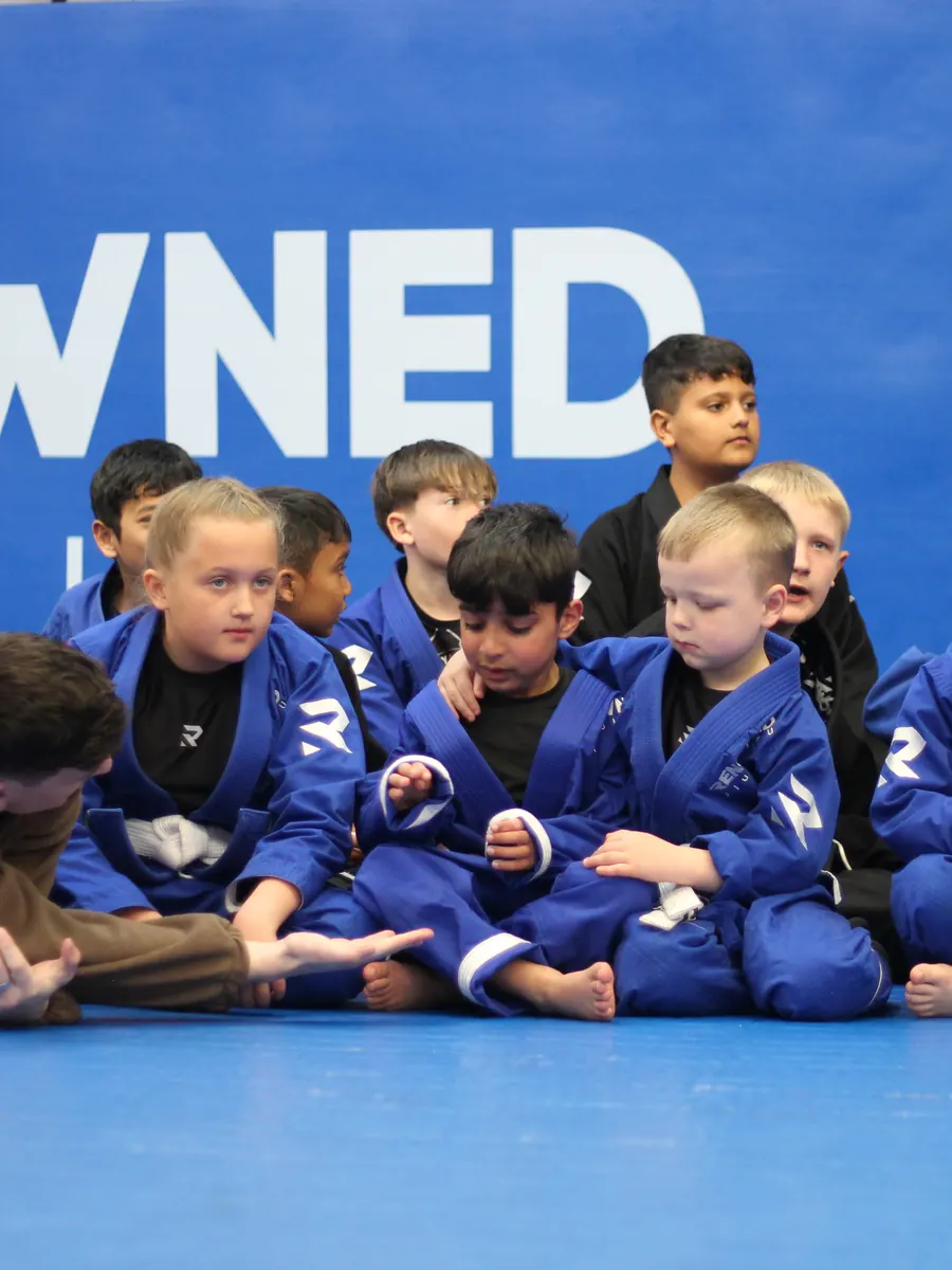A row of children sitting on the mats listening to their coach