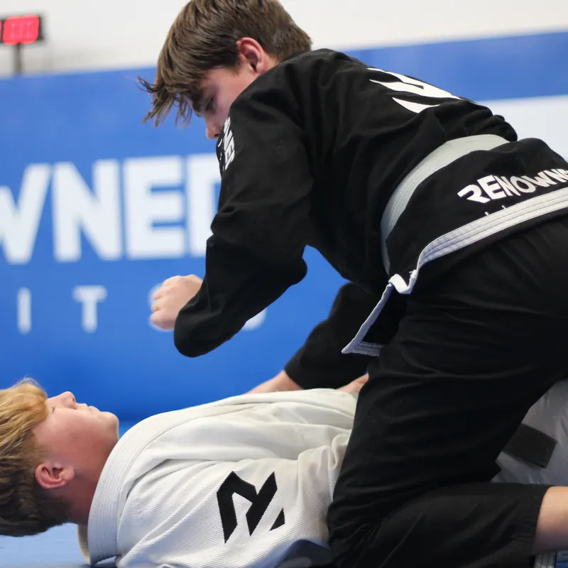 A teenager in a black gi working from the top of a position