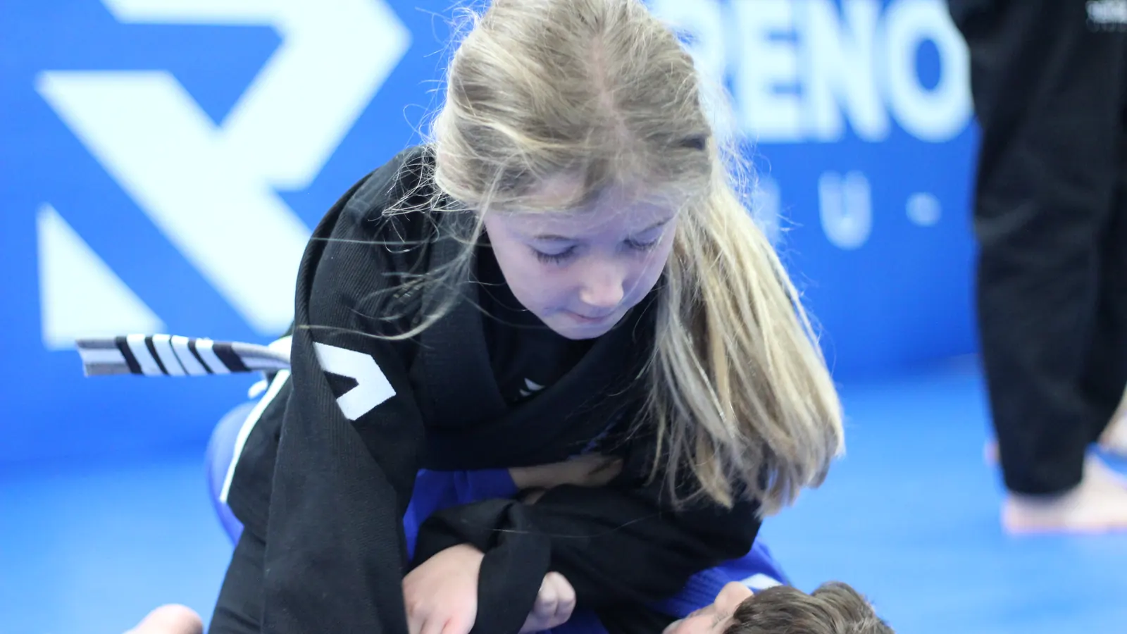 A child in a black gi controlling a position in a kids class