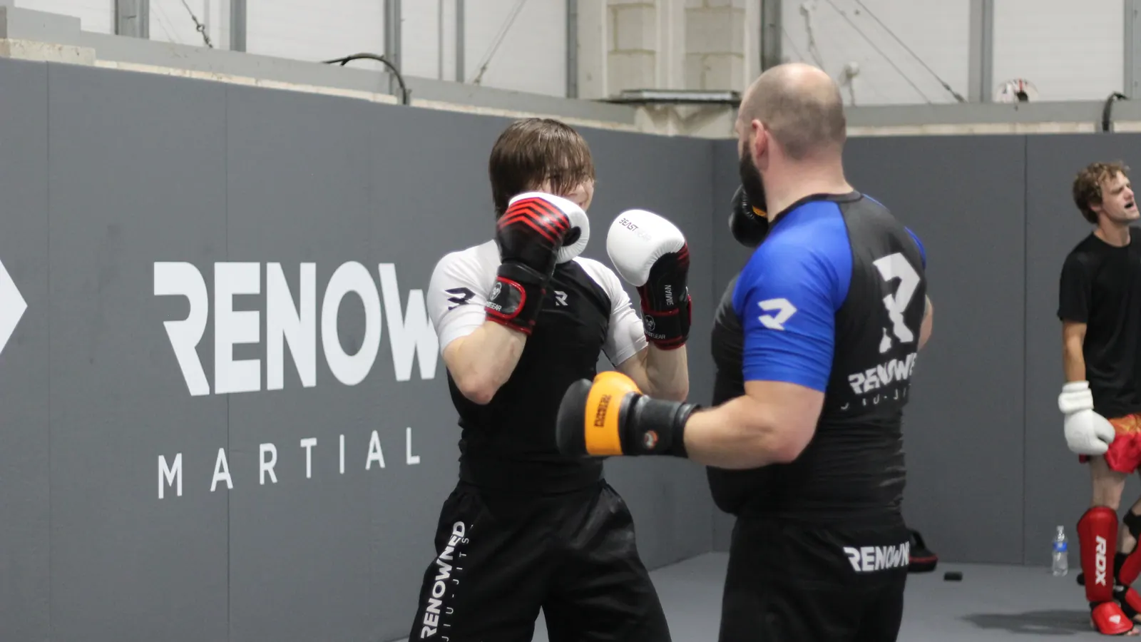 Two adults sparring in gloves while a coach watches